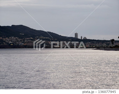 Cloudy coastal horizon featuring distant towers and foreground water enhancing maritime ambiance Cloudy coastal horizon featuring distant towers and foreground water enhancing maritime ambiance 136077945
