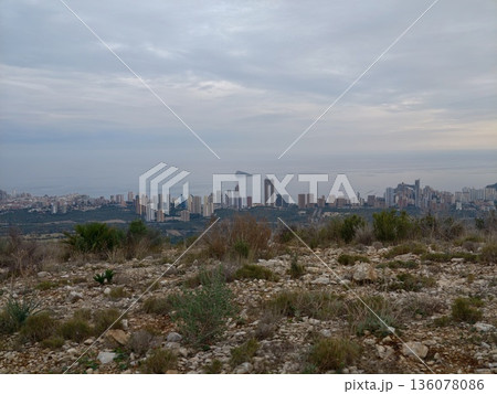 Natural landscape with urban background, Rugged terrain against distant cityscape under overcast skies 136078086