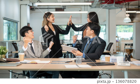 Businesswoman doing high five and man coworkers holding tablet making fist at wooden table in office Businesswoman doing high five and man coworkers holding tablet making fist at wooden table in office 136078820
