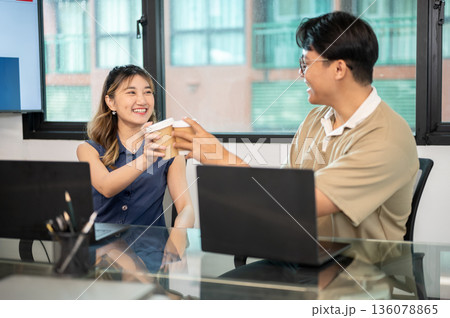 Asian man and woman office workers clinking coffee cup in front of laptop on glass top meeting table 136078865