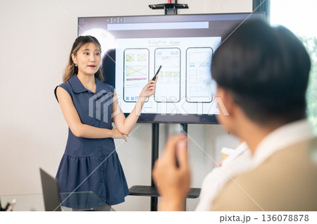 Asian woman pointing pen on monitor presenting mobile app design to coworkers in an office's meeting Asian woman pointing pen on monitor presenting mobile app design to coworkers in an office's meeting 136078878