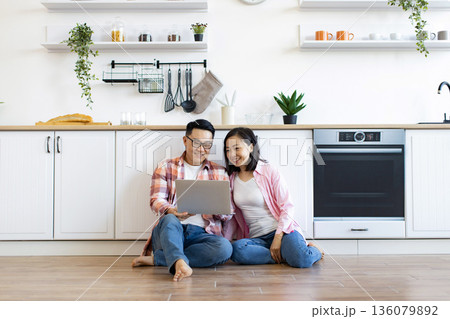 An Asian couple smiles while looking at a laptop computer in their modern kitchen An Asian couple smiles while looking at a laptop computer in their modern kitchen 136079892