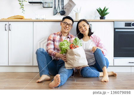 An Asian couple smiles while holding a bag of fresh produce in their modern kitchen An Asian couple smiles while holding a bag of fresh produce in their modern kitchen 136079898