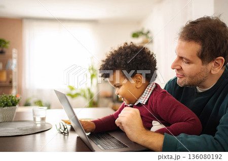 Father hugging son while learning on laptop at home Father hugging son while learning on laptop at home 136080192