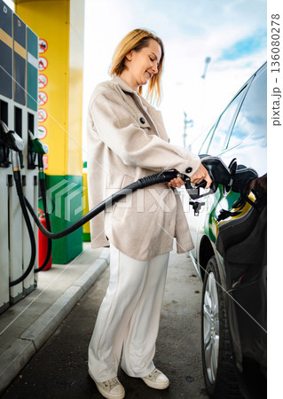 Woman refueling car at gas station pump Woman refueling car at gas station pump 136080278