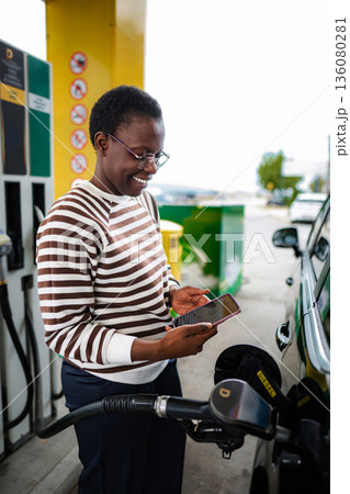 Woman refueling car with diesel using smartphone for payment Woman refueling car with diesel using smartphone for payment 136080281