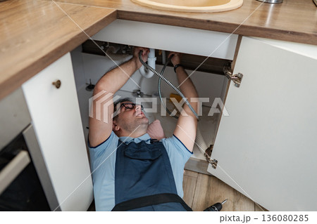 Handyman repairing kitchen sink drain pipe below cabinets Handyman repairing kitchen sink drain pipe below cabinets 136080285
