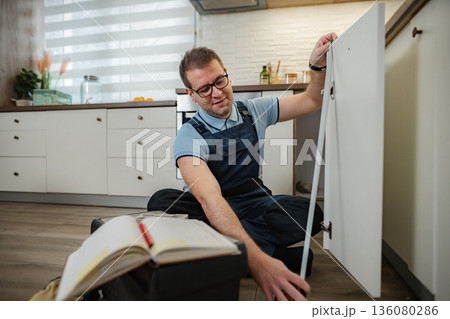 Repairman working on kitchen cabinet door fixing hinges Repairman working on kitchen cabinet door fixing hinges 136080286
