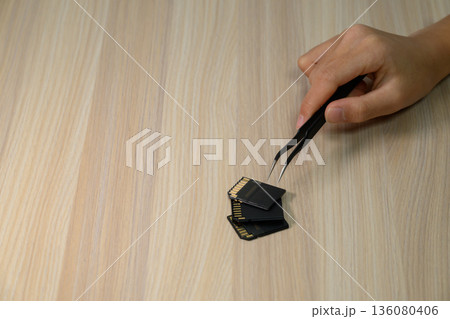 ピンセットでSDカードを扱う手元 136080406