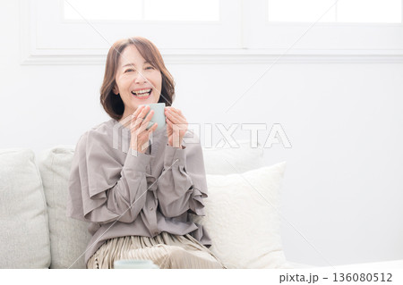 コーヒーカップを持つくつろぐ年配の女性のカメラ目線 コーヒーカップを持つくつろぐ年配の女性のカメラ目線 136080512