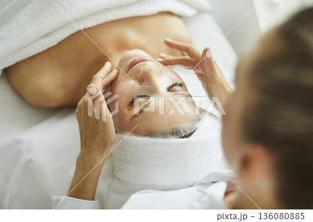 Cosmetologist at a spa salon applies a sheet mask on the face of a relaxed young woman Cosmetologist at a spa salon applies a sheet mask on the face of a relaxed young woman 136080885