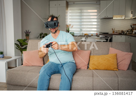 Man playing virtual reality video game on sofa at home 136081417