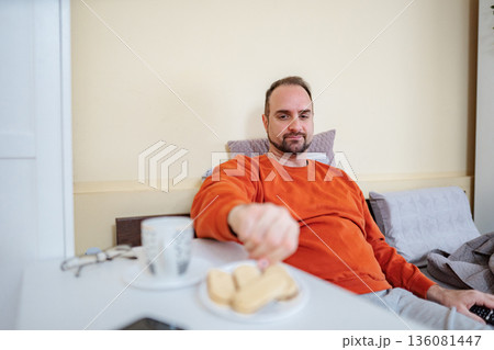Man enjoying breakfast in bed, choosing a biscuit 136081447