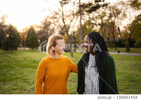 Diverse women friends smiling talking walking in park Diverse women friends smiling talking walking in park 136081458