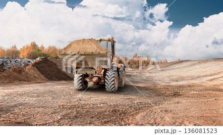 A loader is moving dirt on a construction site during daytime. The scene shows an open area with earth moved and clouds in the sky 136081523