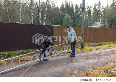 Male workers changing a burnt-out light bulb on light pole and operating at height on roadside utility structure in residential area outdoor scene. Male workers changing a burnt-out light bulb on light pole and operating at height on roadside utility structure in residential area outdoor scene. 136082921