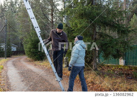 Male workers changing a burnt-out light bulb on light pole and operating at height on roadside utility structure in residential area outdoor scene. Male workers changing a burnt-out light bulb on light pole and operating at height on roadside utility structure in residential area outdoor scene. 136082962