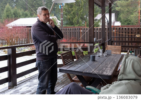 Two adult men arguing on outdoor wooden terrace near house expressing disagreement conflict and strong emotions. Two adult men arguing on outdoor wooden terrace near house expressing disagreement conflict and strong emotions. 136083079