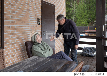 Dialogue aged men in verbal dispute on home porch highlighting tension disagreement communication and relationship issues. 136083081