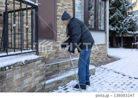 Adult man in winter clothing sweeping snow from porch steps with broom, outdoor home area in cold season maintenance task. Adult man in winter clothing sweeping snow from porch steps with broom, outdoor home area in cold season maintenance task. 136083147