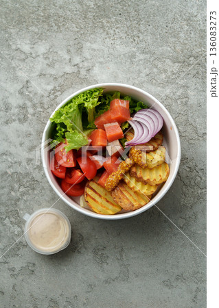 Fresh salad bowl with various vegetables and dressing on a grey stone surface Fresh salad bowl with various vegetables and dressing on a grey stone surface 136083273