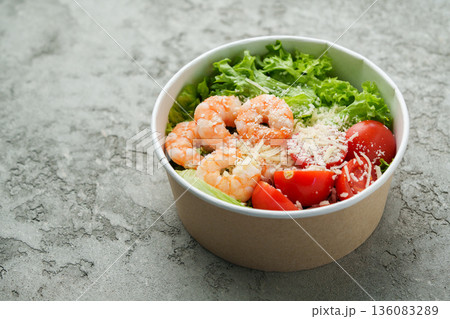 Fresh shrimp salad served in a bowl with lettuce and tomatoes on a gray table 136083289