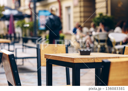People sit at tables on a street while a small dish rests on a nearby table 136083381