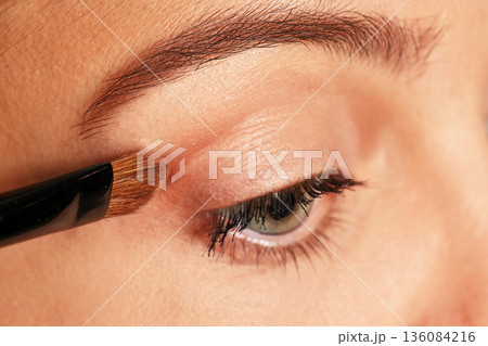 Woman applying cosmetic eyeshadow to her eye using a brush 136084216