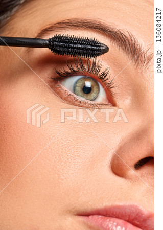 Woman applying black mascara on her eyelashes, focusing on beauty and cosmetics 136084217