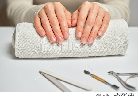 Woman's hands resting on a rolled towel, with manicure tools ready on a white table Woman's hands resting on a rolled towel, with manicure tools ready on a white table 136084223
