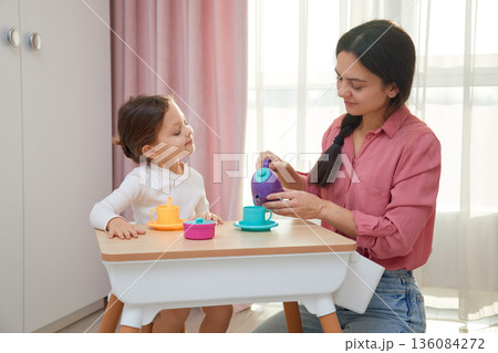 Mother and daughter enjoying a pretend tea party with colorful toy dishes Mother and daughter enjoying a pretend tea party with colorful toy dishes 136084272