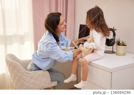 Mother and daughter smiling while interacting in a home office environment Mother and daughter smiling while interacting in a home office environment 136084290