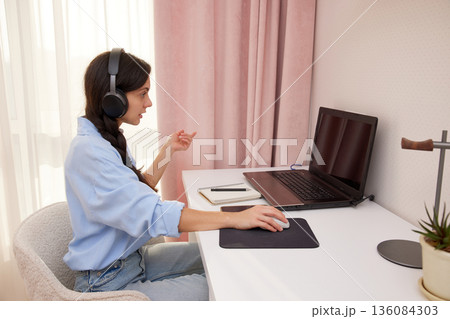Woman wearing headphones and using laptop for online conference 136084303