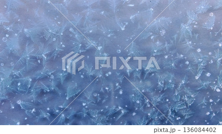 Purple Frost Crystals on Frozen Glass. Delicate Violet Frost Patterns on Window. Stunning macro frost patterns with fern-like ice crystals in violet-purple hues on cold window in winter. Purple Frost Crystals on Frozen Glass. Delicate Violet Frost Patterns on Window. Stunning macro frost patterns with fern-like ice crystals in violet-purple hues on cold window in winter. 136084402