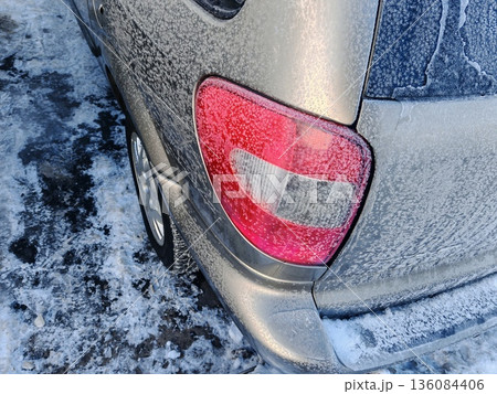 Frost-Covered Car Taillight in Winter Cold. Close-up of red car taillight glowing through thick frost and ice on snowy winter day. Frost-Covered Car Taillight in Winter Cold. Close-up of red car taillight glowing through thick frost and ice on snowy winter day. 136084406