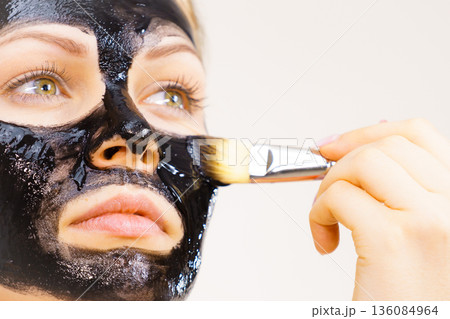 Woman applying black mud mask to face Woman applying black mud mask to face 136084964