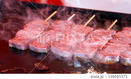 黒い鉄板で焼かれる厚切り牛肉の串焼き 136085571