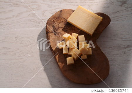 Small block of aged cheese sliced in small pieces on wood board 136085744