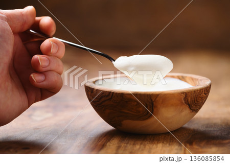 Pov shot of young female hand with full spoon of yogurt sitting at the table 136085854
