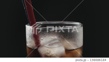 red straw in cola with ice cubes in glass over black background red straw in cola with ice cubes in glass over black background 136086184