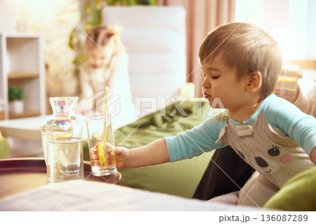 Toddler reaching for glass of water during family time. 136087289