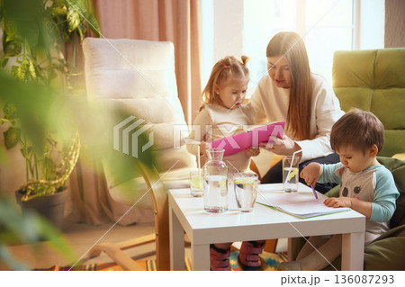 Children drawing and reading at table with mother at home. 136087293