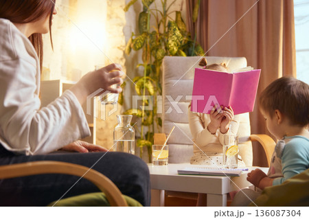 Mother with kids drinking water during quiet family time indoors. 136087304