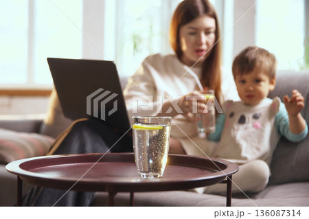 Mother and toddler drinking water with lemon at home. 136087314