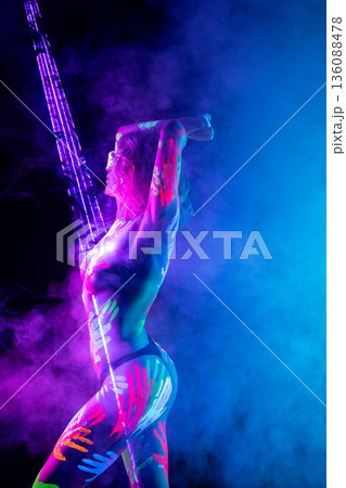 Woman with fluorescent handprint body art posing under UV blacklight in smoke-filled club Woman with fluorescent handprint body art posing under UV blacklight in smoke-filled club 136088478