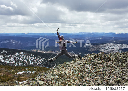 Woman jumping on top of a mountain with arms raised, expressing freedom and joy in natural environment for lifestyle blog 136088957