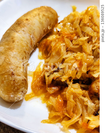 A plate shows a piece of sausage next to a serving of cooked cabbage with vegetables. This meal is prepared for dinner in a home kitchen A plate shows a piece of sausage next to a serving of cooked cabbage with vegetables. This meal is prepared for dinner in a home kitchen 136089525