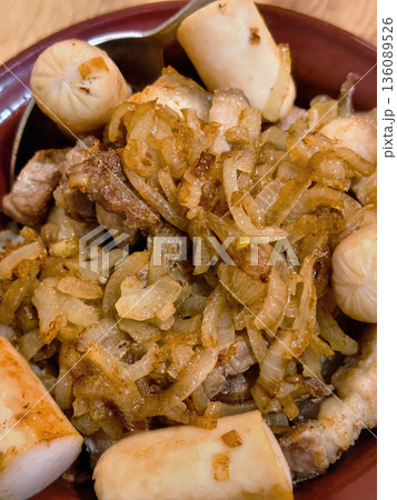 Slices of grilled meat with cooked onions and small sausages are served in a bowl on a dining table in the evening setting Slices of grilled meat with cooked onions and small sausages are served in a bowl on a dining table in the evening setting 136089526