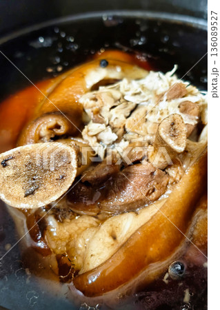 Pork meat and bones are simmering in a pot on a stove. The heat brings out flavors as the dish cooks slowly in a home kitchen during the evening hours 136089527
