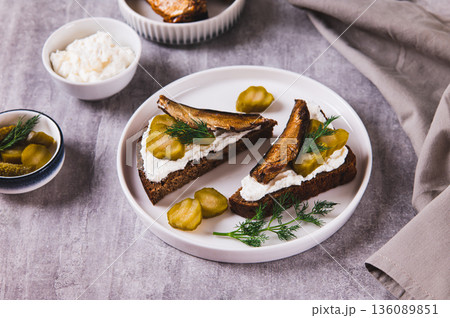 Rye bread toasts with cream cheese, sprats and pickles on a plate on the table Rye bread toasts with cream cheese, sprats and pickles on a plate on the table 136089851